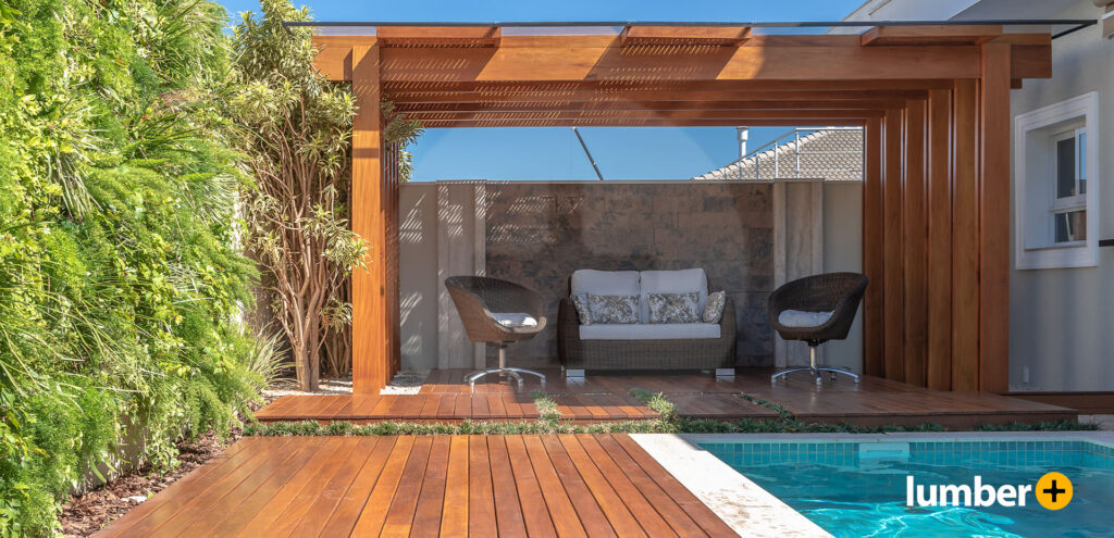 Warm red wooden decking and pergola next to a swimming pool. 