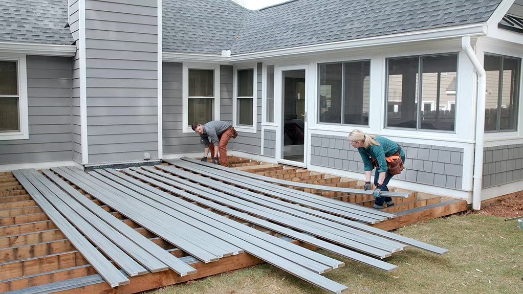 Two workers lay out Trex composite decking for installation behind the house.