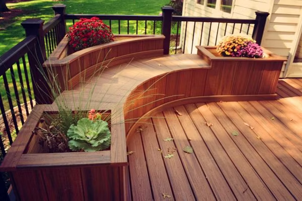 Trex patio deck in reddish-brown with a built-in curved bench and decorative flowerpots, highlighting Trex deck bench ideas for a cozy outdoor design.